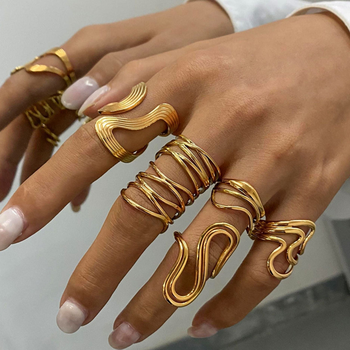 Hand wearing multiple Charming Curves 18K gold plated sculptural wave rings