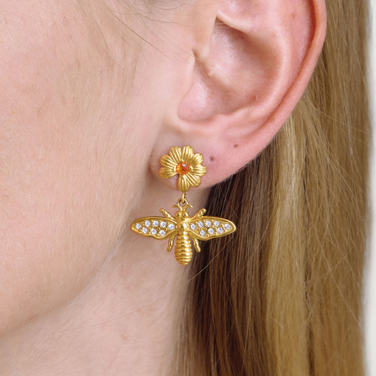Gold bee-shaped earring with a flower detail worn by a person.