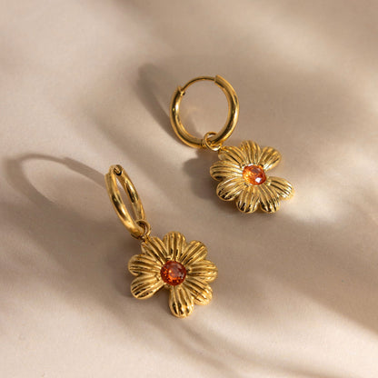 Pair of gold daisy huggie hoop earrings made of tarnish-free stainless steel with warm amber crystal centers on an off-white ceramic dish