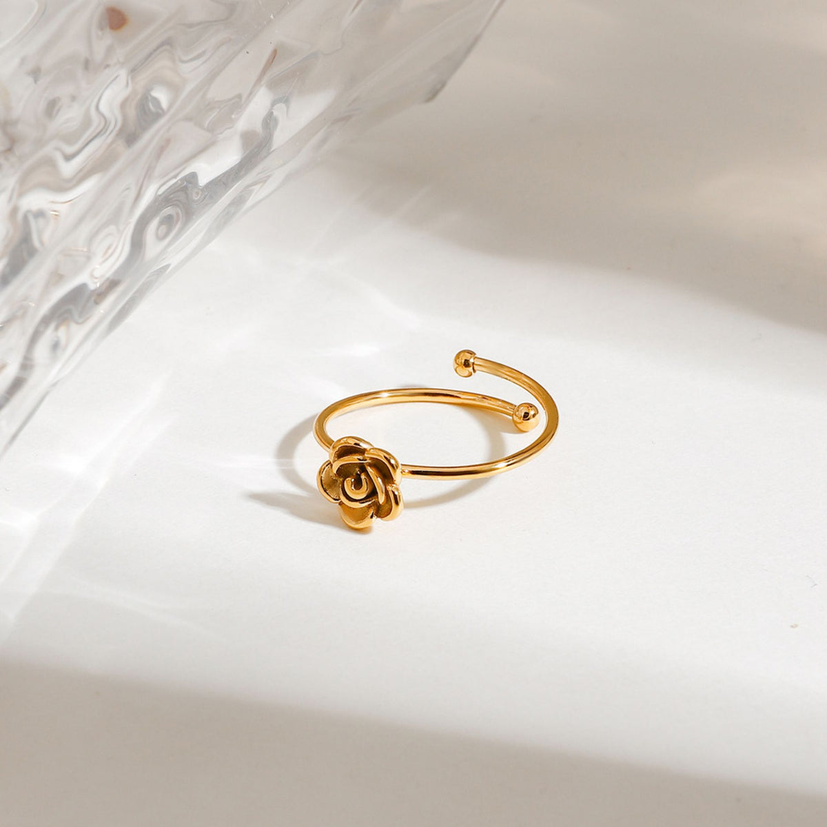 Top-down view of adjustable gold stainless steel flower wrap ring with sculpted rose petal detail next to fluted glass dish