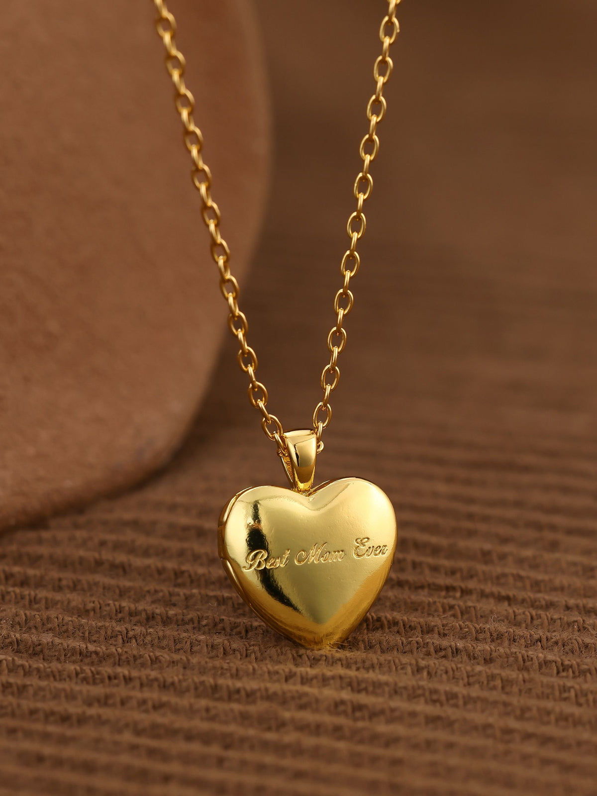 Gold heart-shaped locket pendant necklace on a brown textured background