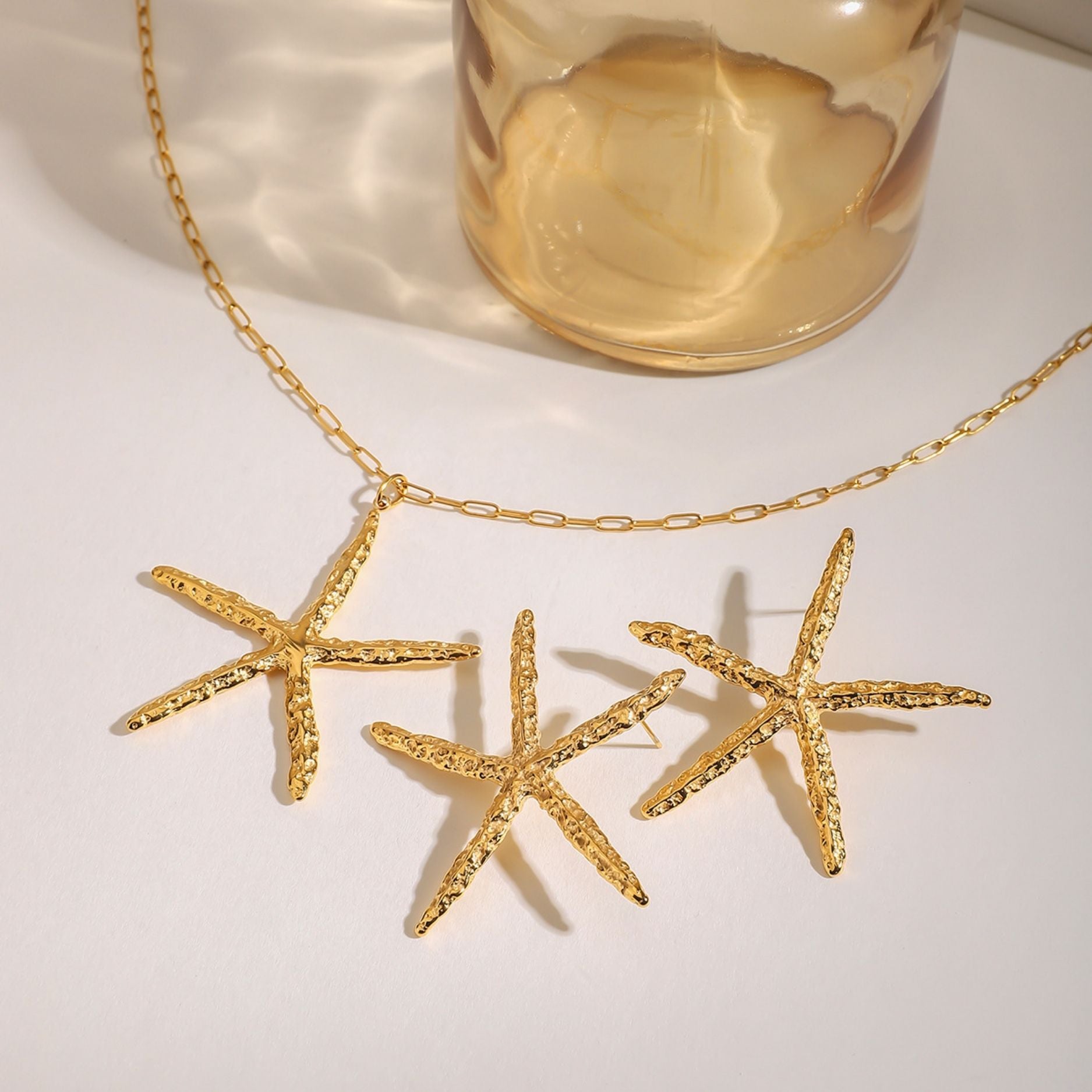 Waterproof gold stainless steel hammered starfish necklace and matching earrings set displayed on a white surface with sea shells